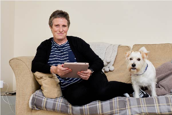 Emma sat using ipad on sofa with white dog