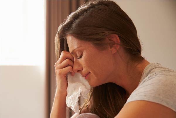 Lady with brown hair crying with hand holding a tissue
