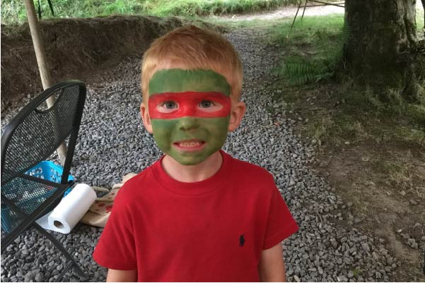 Small male child smiling with face painted green and red.