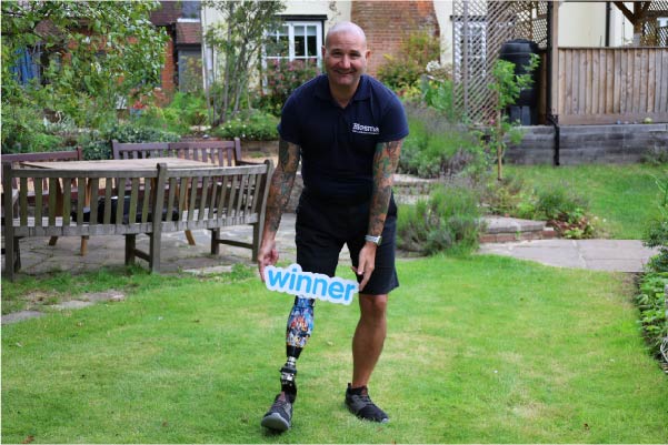 Limbless Veteran in a hospice garden holding a winner sign over his prosthetic leg.
