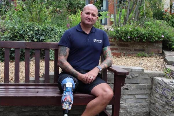 Limbless Veteran man sat on a bench in hospice garden with prosthetic leg.