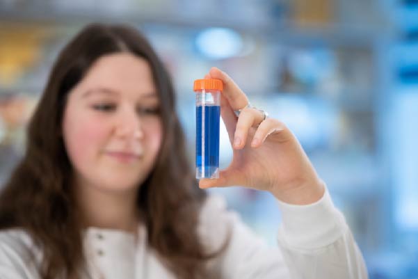 lady scientist in a lab coat holding a test tube with blue liquid