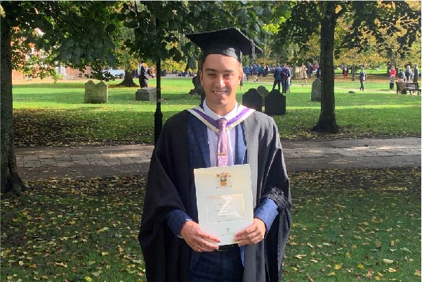 Alex in cap and gown at his graduation holding his degree