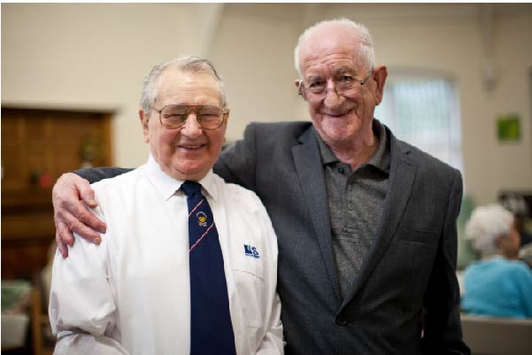 Old men standing together with their arms round each other smiling